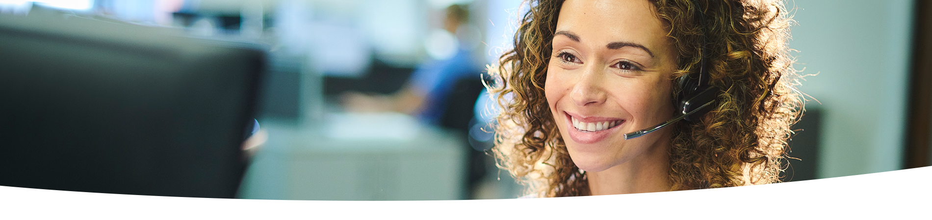 Woman wearing headset and hospital scrubs, seated at a desk.