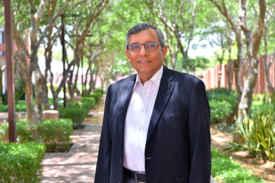 Dr. Zulfiqar Bhutta stands outside on a tree-lined path.